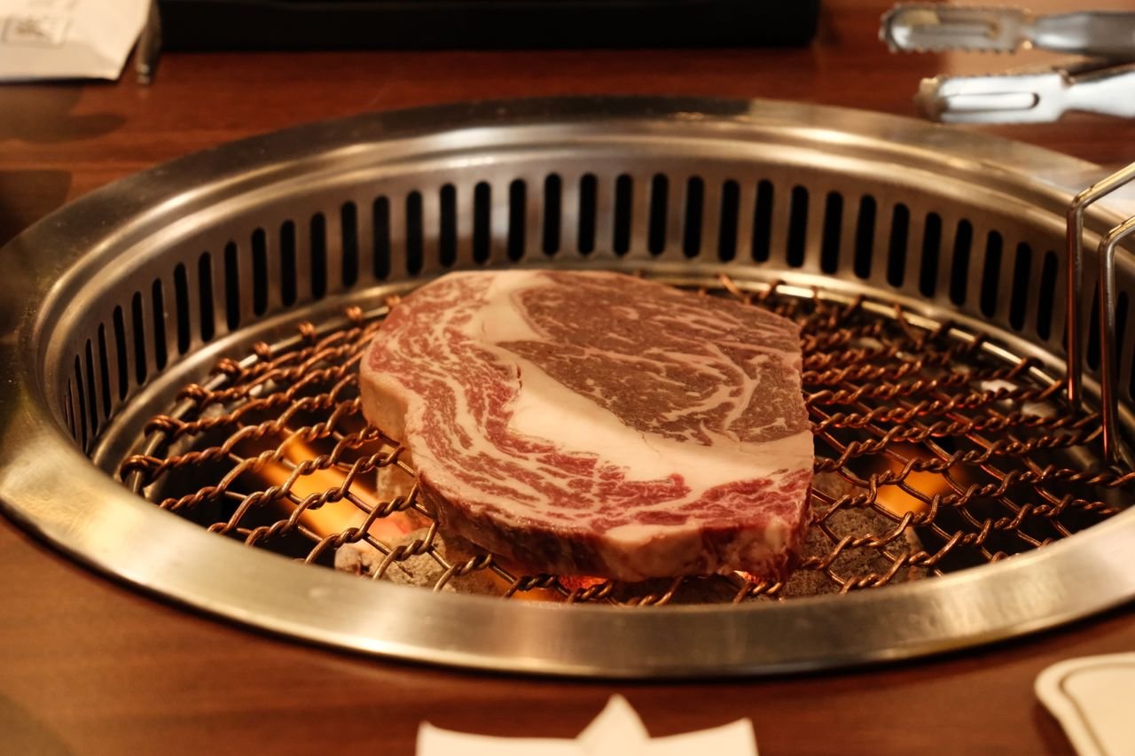 The Art of Drawing Readers In: Your attractive post title goes here Close-up of marbled beef steak grilling on a Korean barbecue, showcasing its texture.