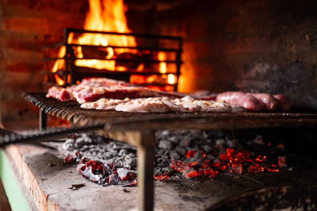 A warm close-up view of meats grilling over fiery coals on a barbecue, creating a cozy cooking ambiance.