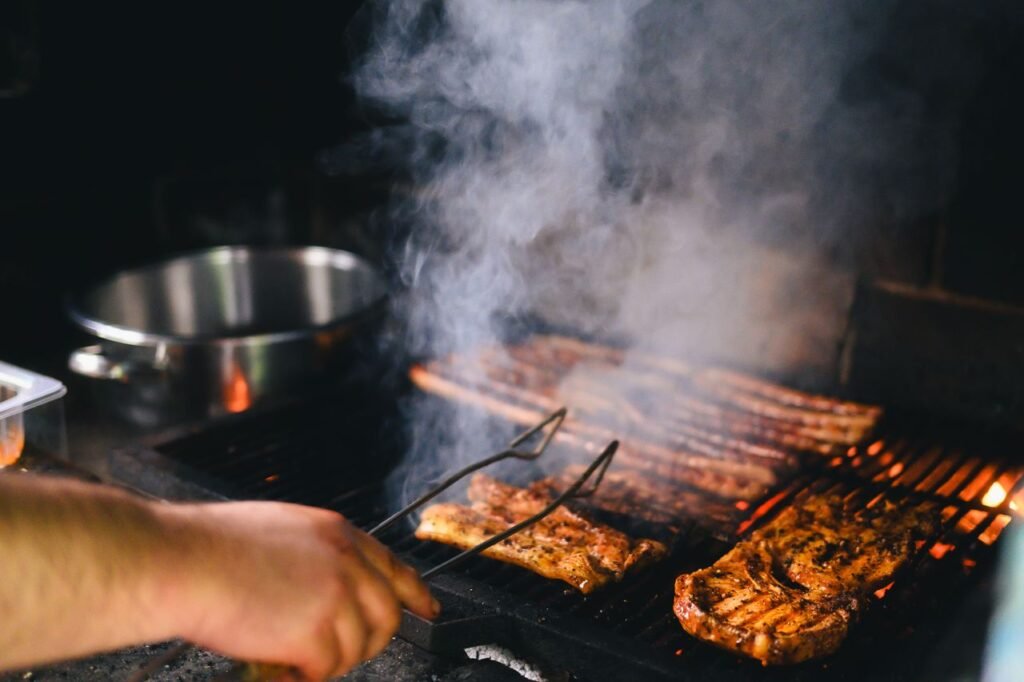 Close-up of grilling meat with smoke rising on a barbecue, outdoors.