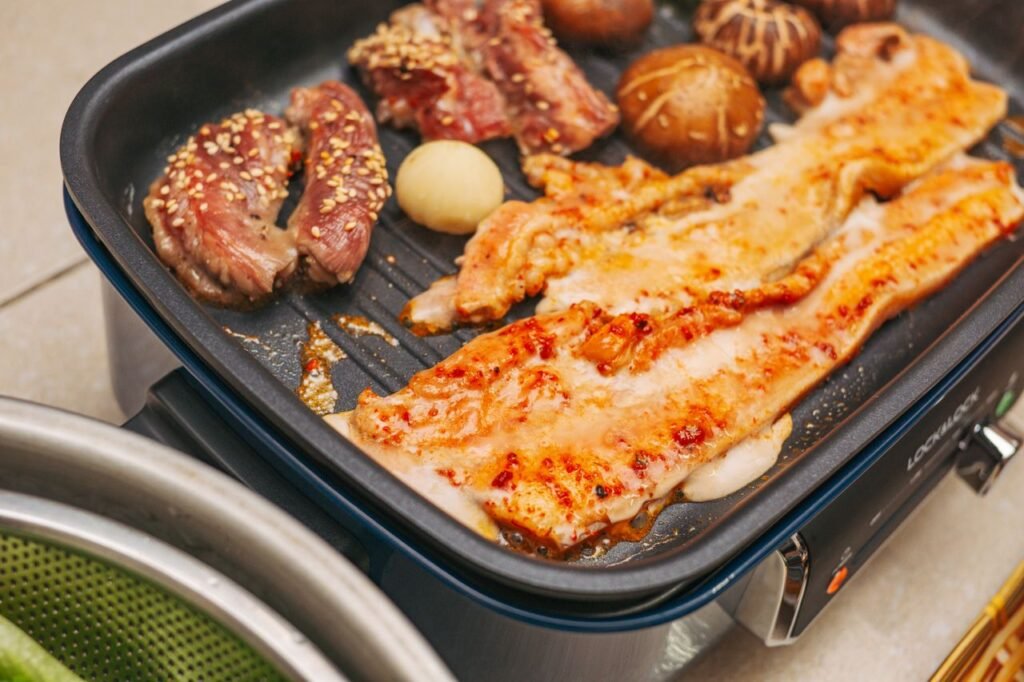 Delicious Korean BBQ with pork belly, beef, mushrooms, and garlic sizzling on an electric grill.